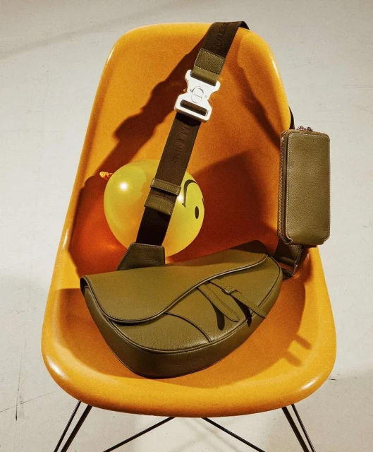 Saddle bag with strap over mustard-yellow molded plastic chair. Bag has an olive-green pouch and yellow balloon with a smiley face in the background.