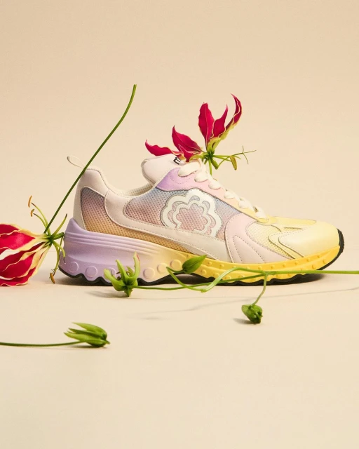 Fashionable pastel-colored sneaker is displayed against a neutral background and adorned with vibrant red Gloriosa superba lilies.