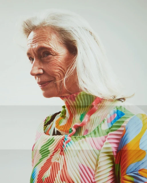 Elegant older woman in pleated dress. Portrait of a senior female with white hair wearing patterned top in light, airy studio setting.