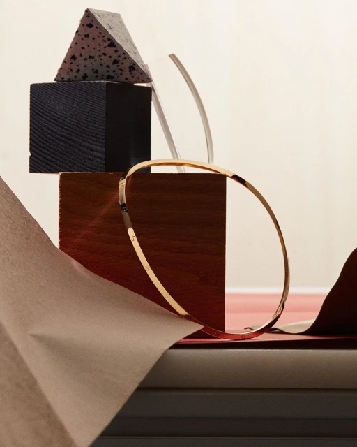 Still life featuring a gold bangle bracelet displayed on wooden and stone geometric blocks, complemented by craft paper.