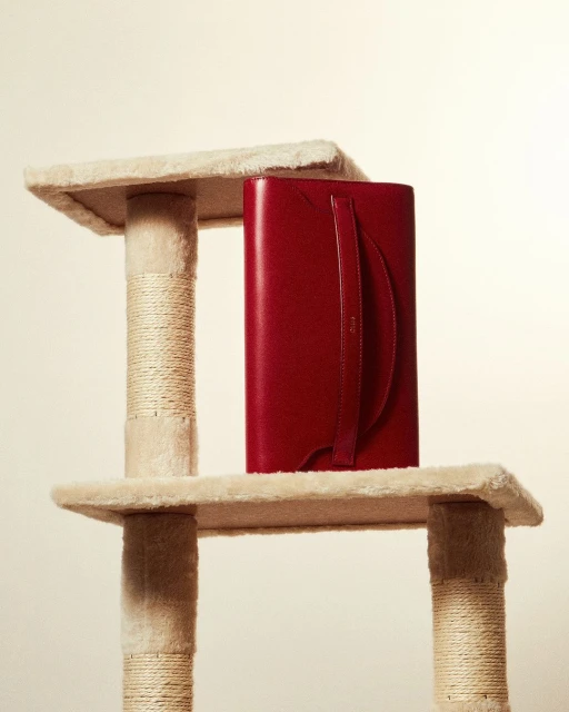 Red leather agenda on a carpeted cat tree, presenting a juxtaposition of luxury and pet products in a brightly lit indoor setting.