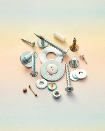 Close-up of various silver-toned metal screws, nuts, bolts, washers, and fasteners scattered on a gradient peach and light green surface.