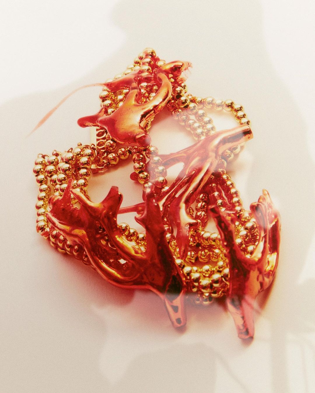 Artistic close-up photograph of an abstract, metallic gold-colored object with branching shapes on a light neutral surface.