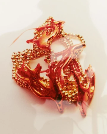 Artistic close-up photograph of an abstract, metallic gold-colored object with branching shapes on a light neutral surface.