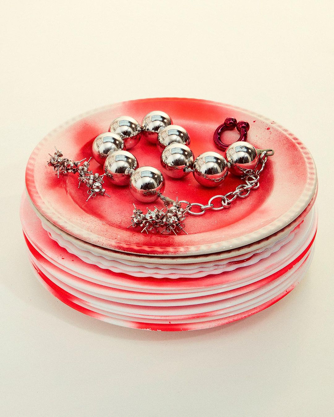 Silver ball and spike bracelet on a stack of red and white plates. Jewelry fashion shot in a studio setting.