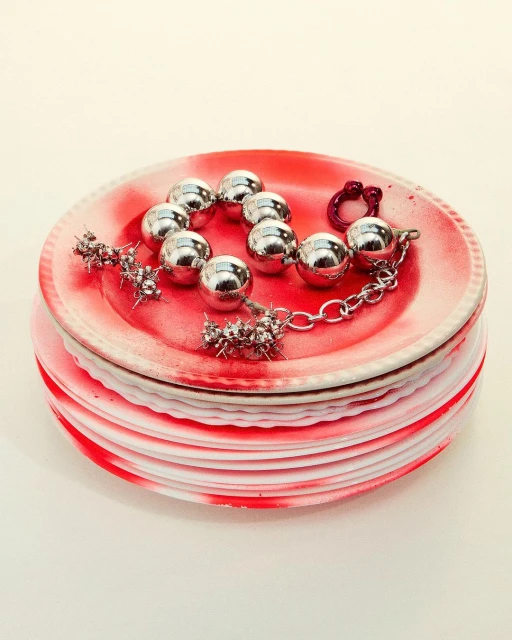 Silver ball and spike bracelet on a stack of red and white plates. Jewelry fashion shot in a studio setting.