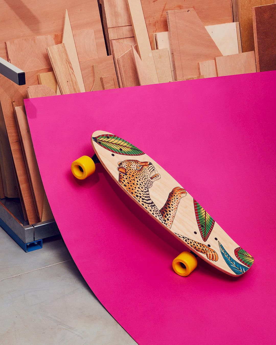 Leopard print skateboard with yellow wheels on a pink surface against a wooden background, photographed in studio lighting.