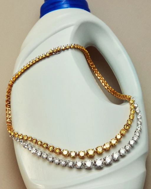 Two tennis necklaces, one gold and one silver, are draped across the top of a white and blue detergent bottle indoors with neutral background.