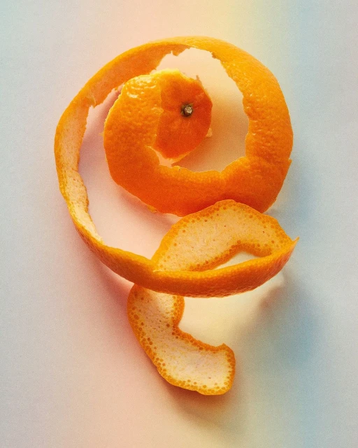 Close-up of an orange peel spiraling around, creating a visually appealing and artistic food still life on a soft gradient background.