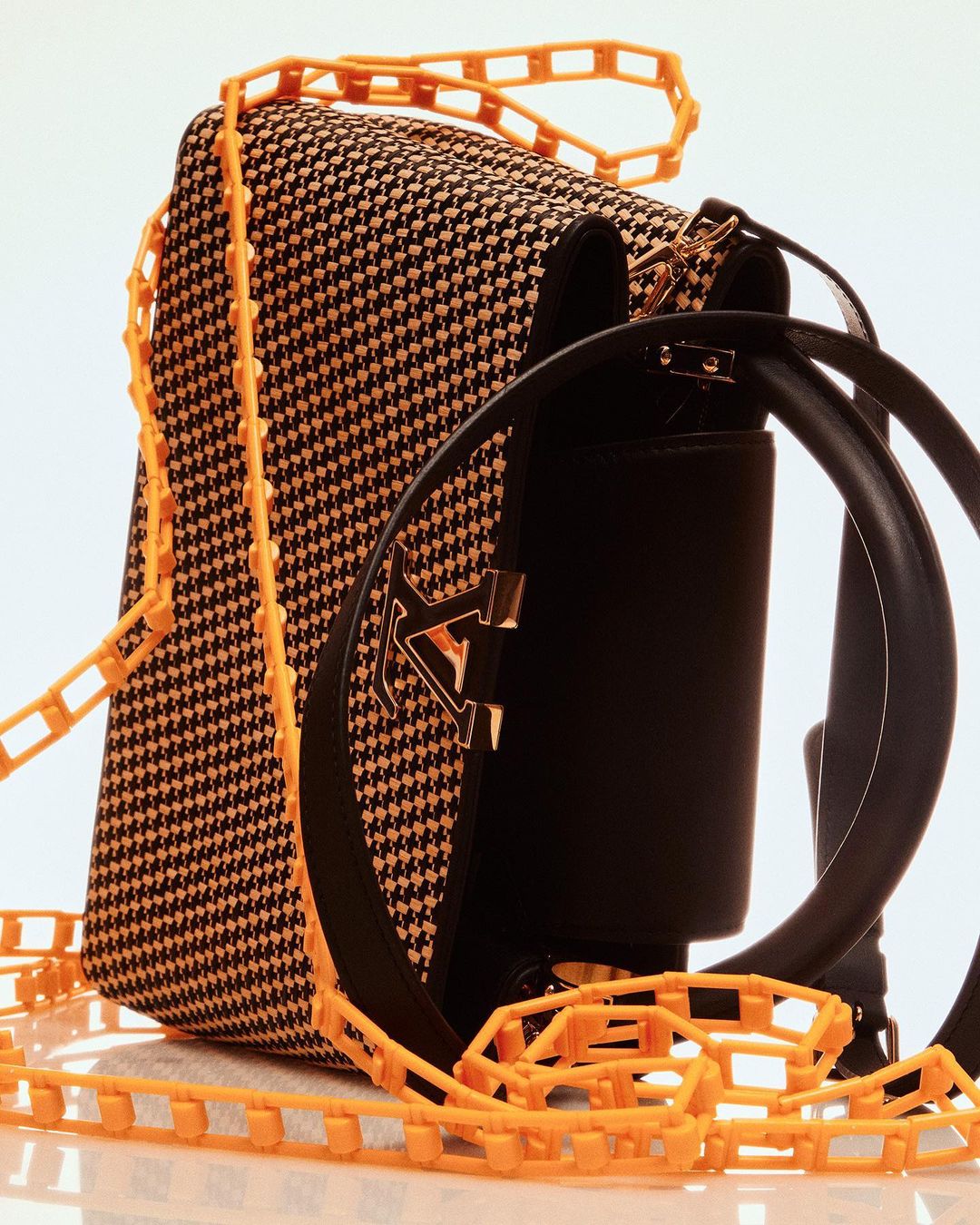 Houndstooth patterned satchel bag with orange plastic chain strap and black leather accents isolated on a white background.