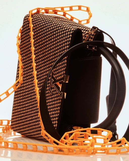 Houndstooth patterned satchel bag with orange plastic chain strap and black leather accents isolated on a white background.