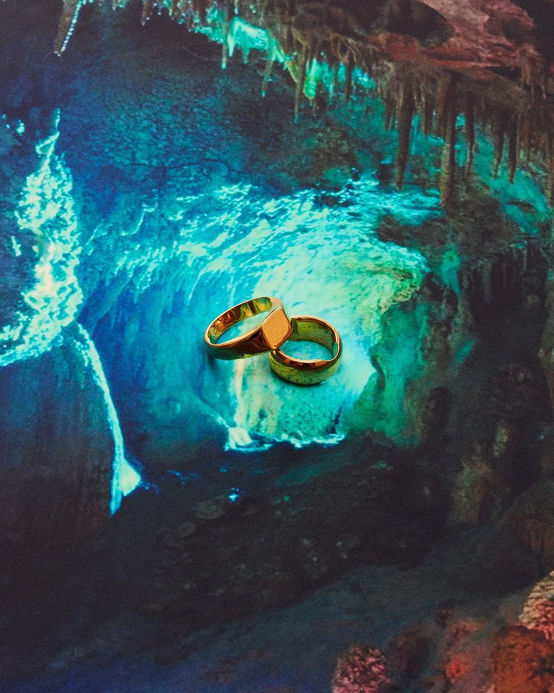 Two golden rings are placed in the center of a photo, which has a vibrant, cave-like pattern with blue and green colors in the background.