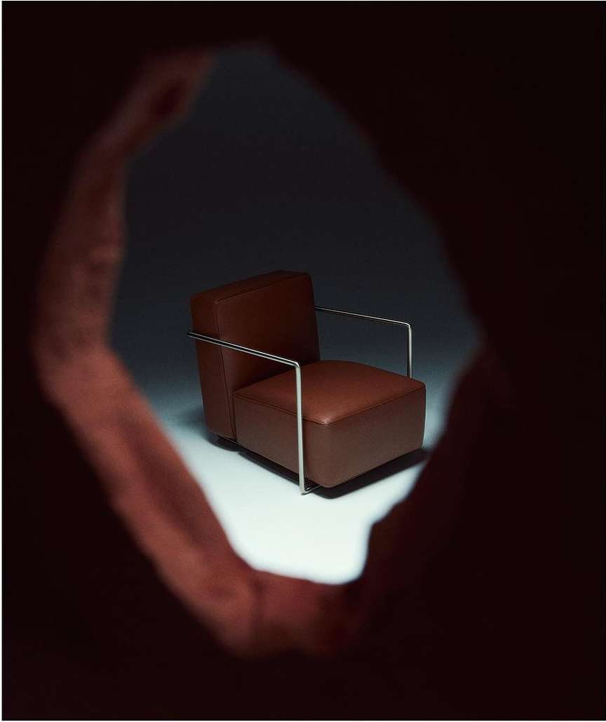 Brown leather armchair with metal frame, presented in a spotlight through a textured hole, creating an intimate and focused composition.