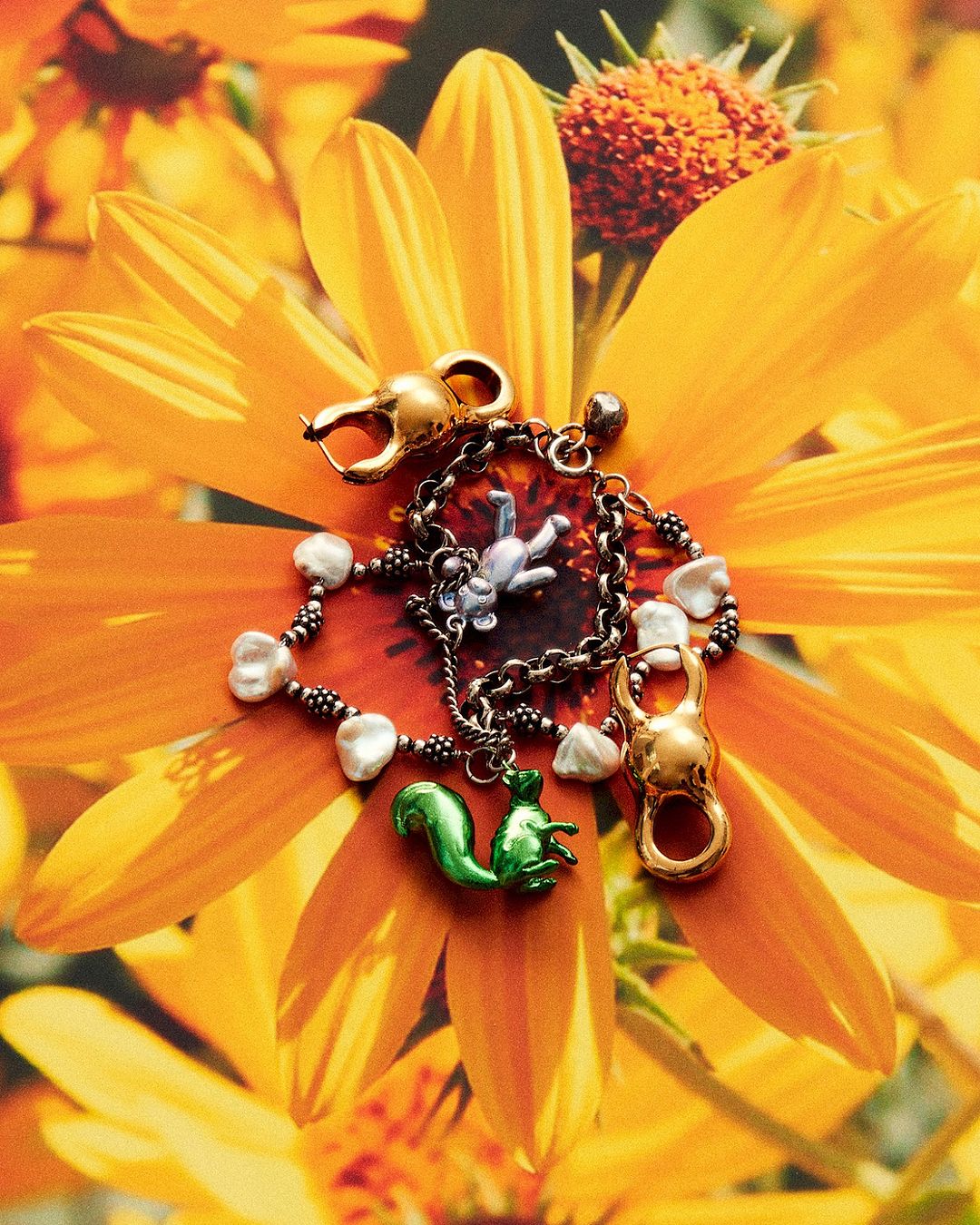 Close-up of a decorative chain bracelet with charms, including a squirrel and a figure, set against a vibrant yellow flower.