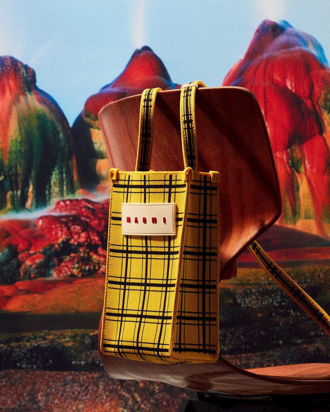 Yellow plaid bag with a wooden handle on a chair, set against a backdrop of fantastical red and orange mountains.
