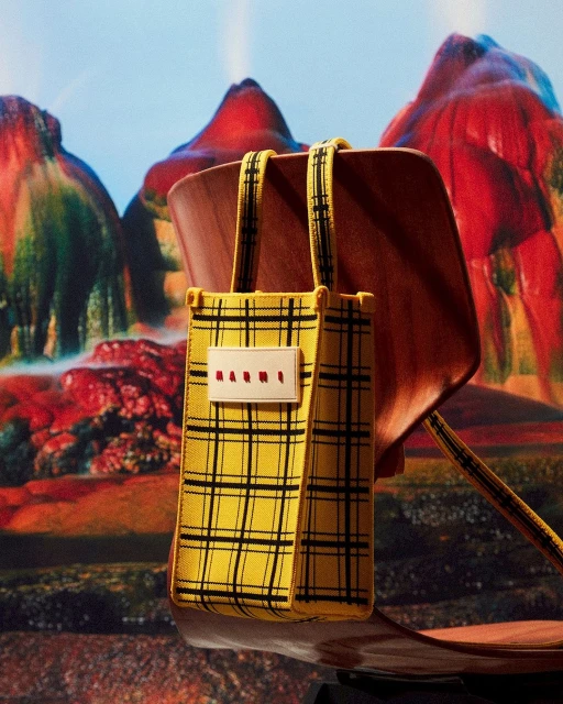 Yellow plaid bag with a wooden handle on a chair, set against a backdrop of fantastical red and orange mountains.
