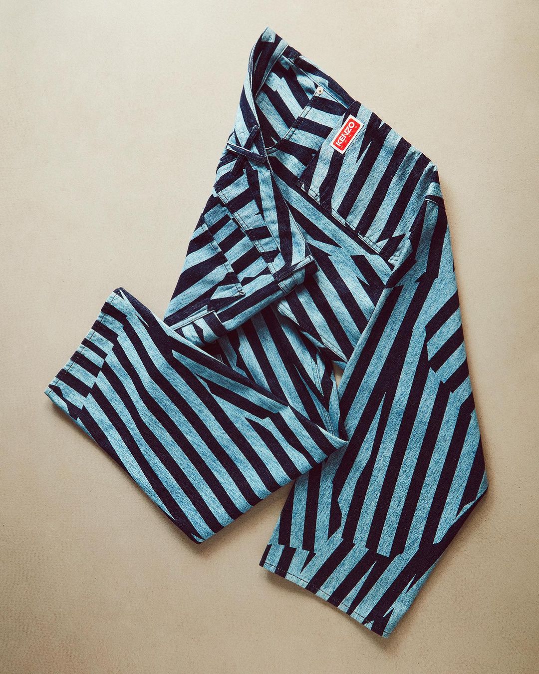 Folded blue and black striped pants by Kenzo on a neutral surface, creating a visually appealing fashion still life image.