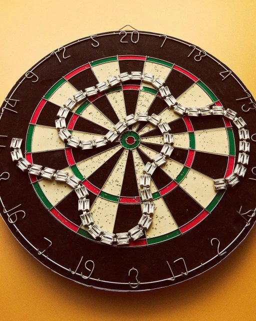 Close-up of dartboard with sparkling necklace in center, creating a target fashion-art still life on a yellow wall.