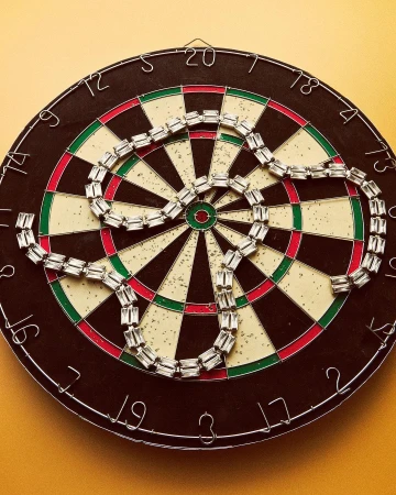 Close-up of dartboard with sparkling necklace in center, creating a target fashion-art still life on a yellow wall.