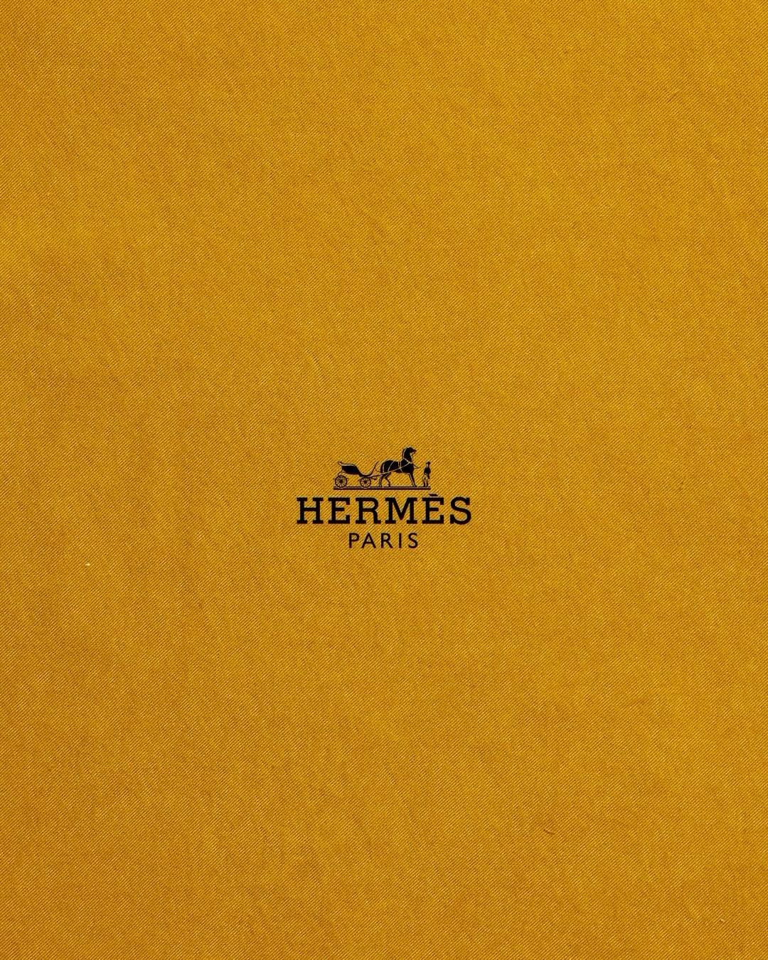 Close-up of the Hermès Paris logo on a yellow-gold textured background, showcasing the iconic horse-drawn carriage emblem.