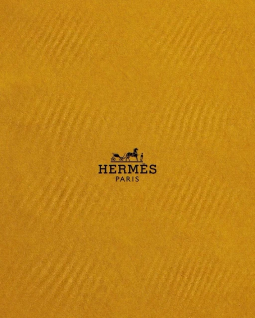 Close-up of the Hermès Paris logo on a yellow-gold textured background, showcasing the iconic horse-drawn carriage emblem.