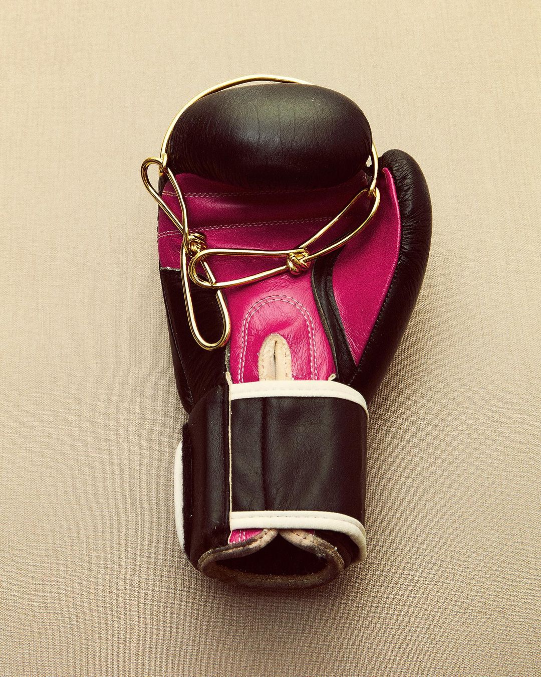 Overhead shot of black and pink boxing glove with gold strings on neutral background, close-up of sports equipment, no people visible.