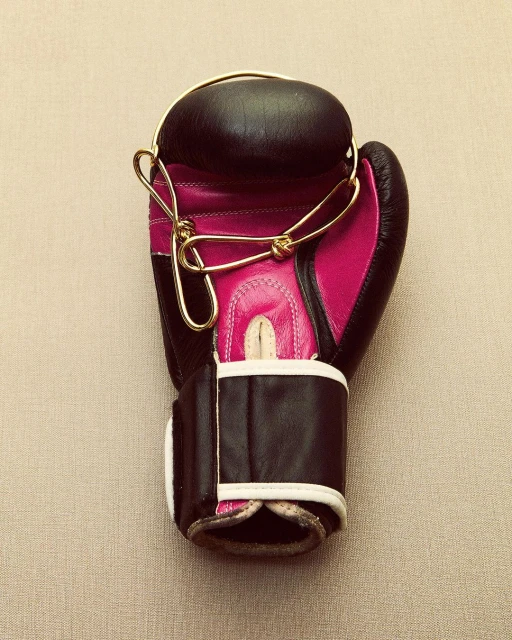 Overhead shot of black and pink boxing glove with gold strings on neutral background, close-up of sports equipment, no people visible.