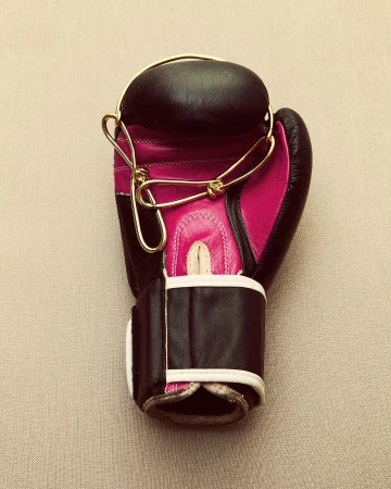 Overhead shot of black and pink boxing glove with gold strings on neutral background, close-up of sports equipment, no people visible.