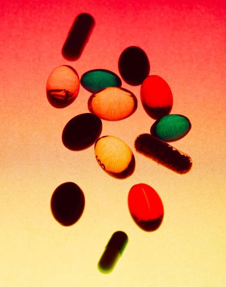 Macro studio shot of colorful oblong and circular pills on a gradient background of peach, orange, pink, and yellow tones.