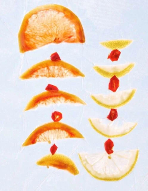Citrus slices arranged in a stacked pattern, featuring grapefruit and lemon halves, each topped with a vibrant red berry accent.