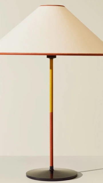 Minimalist table lamp featuring a conical cream shade with tan trim and a two-tone yellow and tan stand on a circular black base.