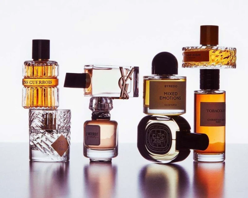 Arrangement of multiple perfume bottles with various designs and amber-colored liquids against a white background in a studio setting.