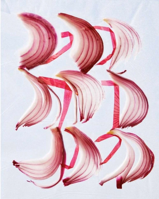 Overhead view of sliced red onion pieces arranged on a white surface with red ribbon creating geometric pattern; food photography.