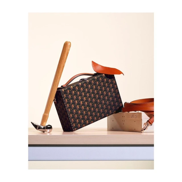 Luxury leather handbag with a geometric pattern next to a hammer, leather swatch, and wooden block, creating a high-fashion studio product shot.
