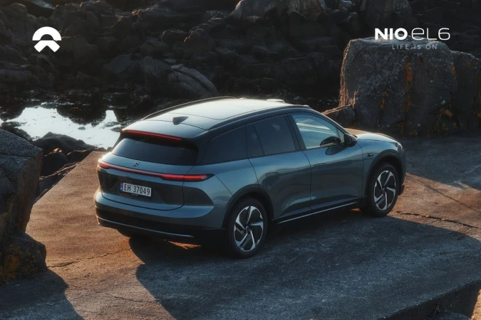 Electric blue NIO EL6 SUV on a rocky coastal landscape with diffused sunlight. Automotive photography featuring a contemporary car design.