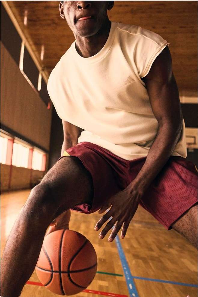 African-American man in athletic wear dribbles a basketball on a wooden court, indoor gymnasium, action shot.