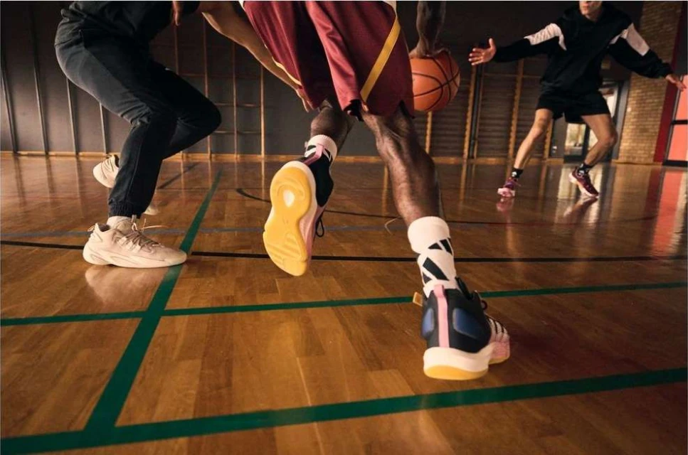 Low angle shot of basketball players dribbling and moving on a hardwood court with green lines in a gymnasium.