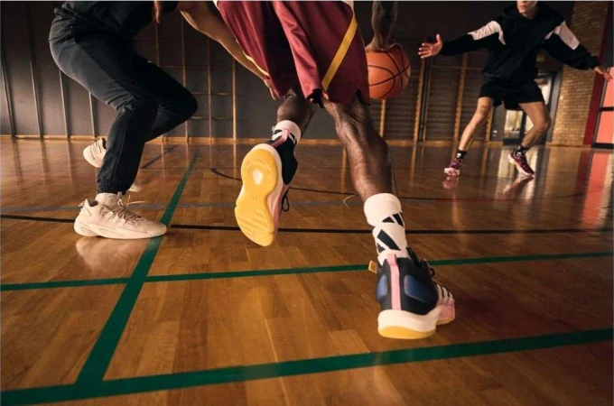 Low angle shot of basketball players dribbling and moving on a hardwood court with green lines in a gymnasium.