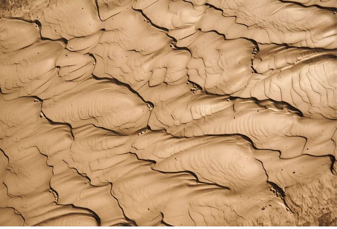 Textured sand ripples create a mesmerizing pattern across the frame, showcasing the intricate details and subtle shadows of a sandy landscape.