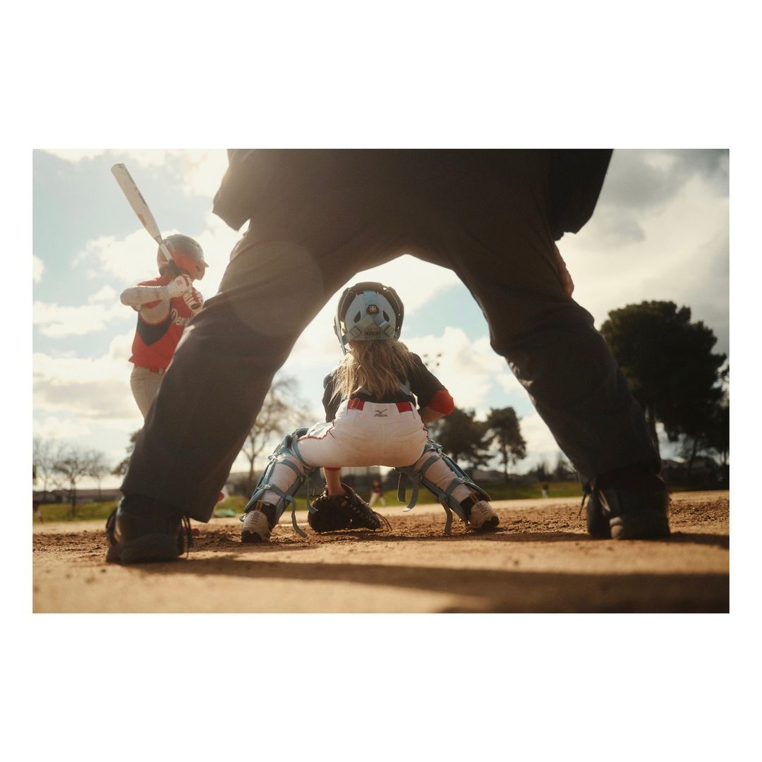 Youth baseball game with a batter swinging, catcher ready, and umpire observing the action on a sunny day on a dirt field.