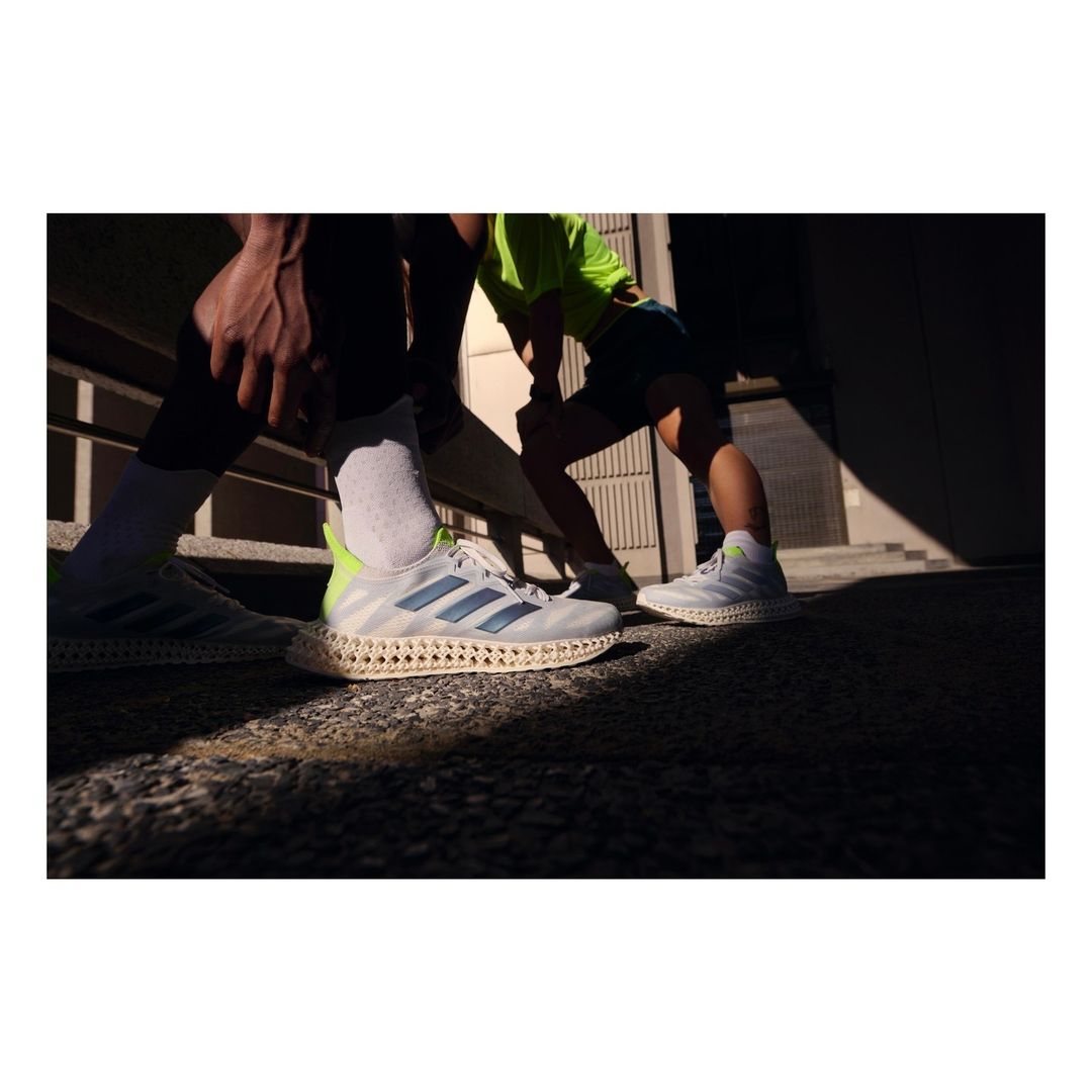 Three people wearing athletic shoes, captured in an outdoor urban setting with bright sunlight creating shadows on the ground.
