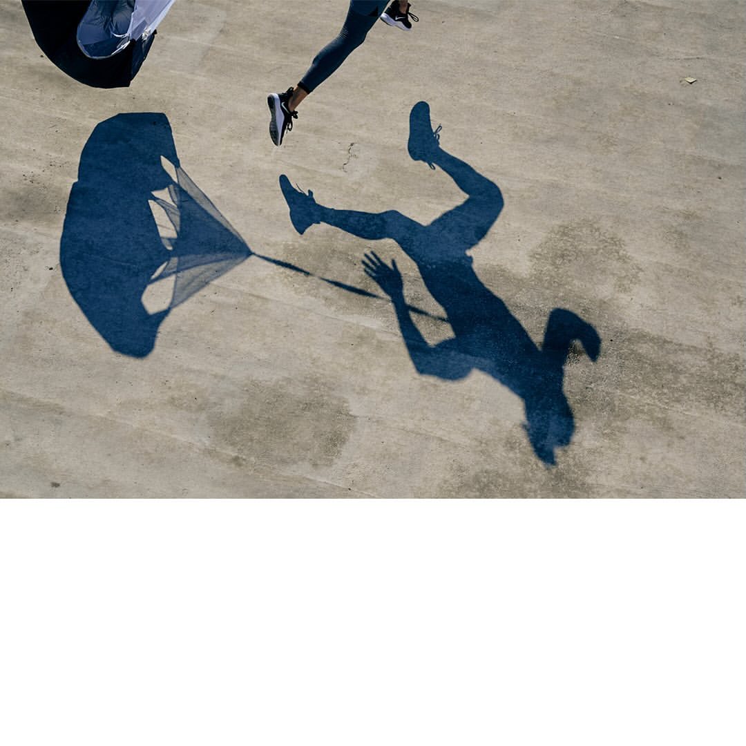 High-angle shot of runner's shadow with parachute, highlighting strength and endurance in a dynamic, minimalist composition.