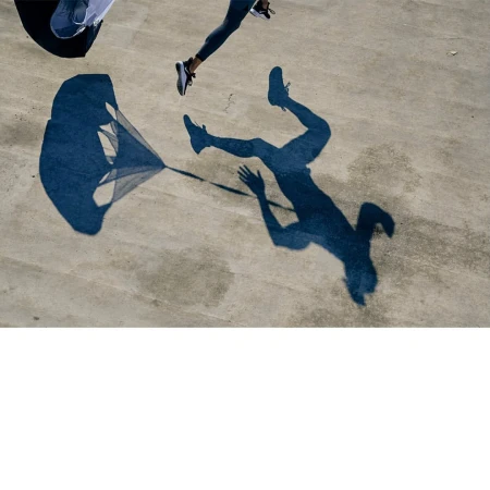 High-angle shadow capture of a runner in motion with a trailing parachute on a textured concrete surface.