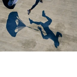High-angle shadow capture of a runner in motion with a trailing parachute on a textured concrete surface.