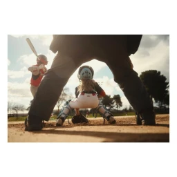 Low angle view through umpire legs of a youth baseball catcher crouching behind home plate with batter in background