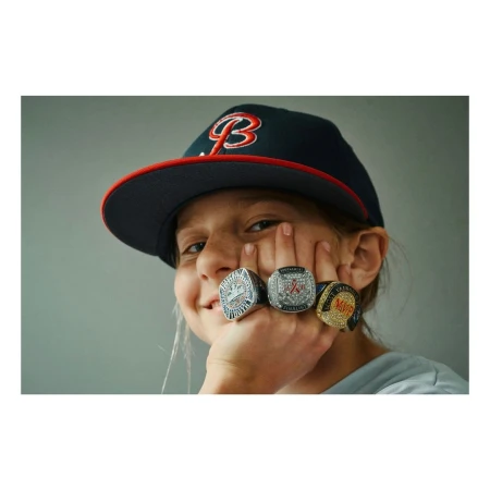 Close-up portrait of a child wearing a baseball cap and four championship rings across their fingers by photographer Florian Bison.