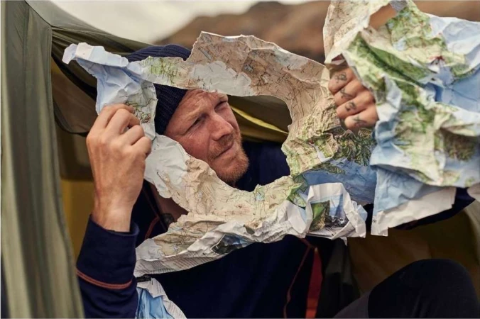 Man looking through a torn topographic map inside a camping tent, photographed by Florian Bison