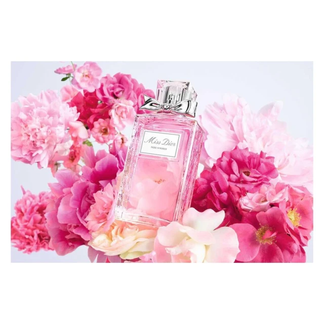 Elegant still life featuring a 'Miss Dior' perfume bottle with a silver bow, surrounded by vibrant pink peonies against a white backdrop.