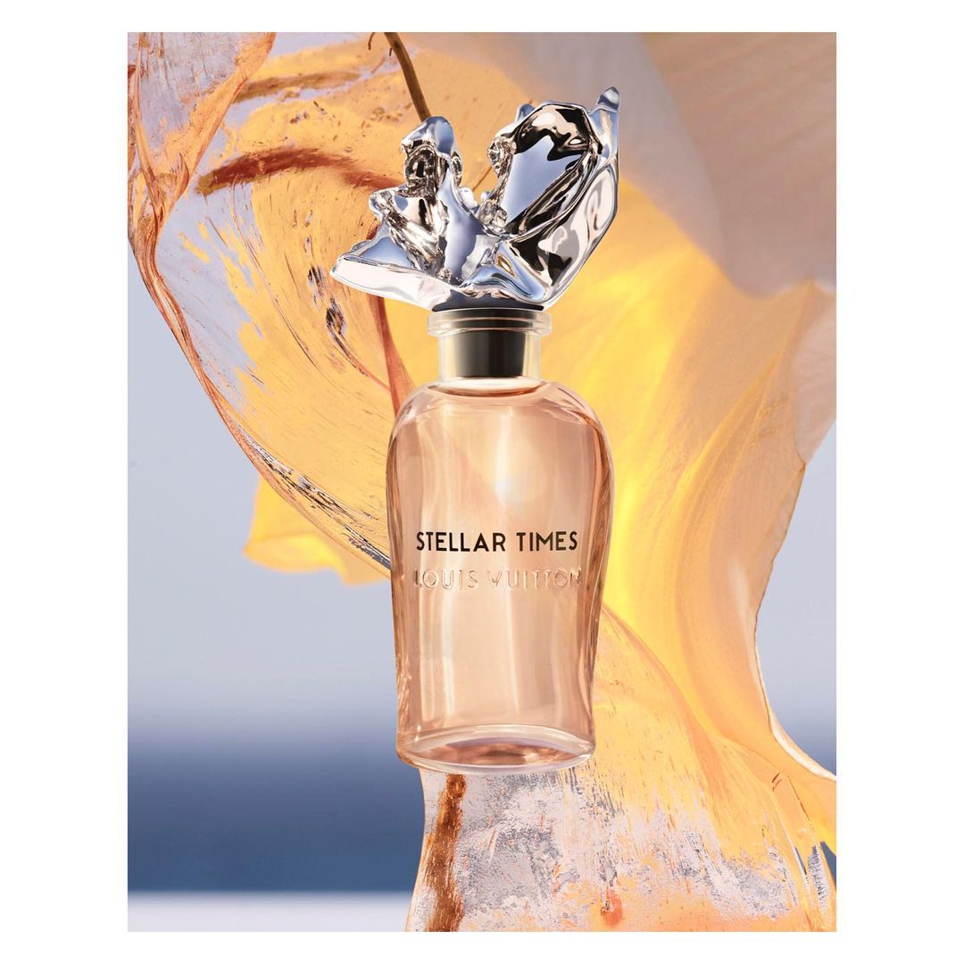 Louis Vuitton Stellar Times perfume bottle featuring a metallic, figurative topper against a light blue and orange abstract background.