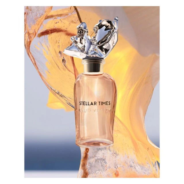 Louis Vuitton Stellar Times perfume bottle featuring a metallic, figurative topper against a light blue and orange abstract background.